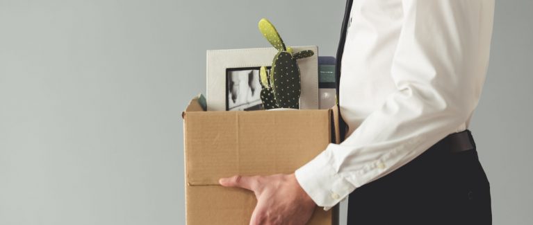Getting fired. Cropped image of handsome businessman in formal wear holding a box with his stuff, on gray background