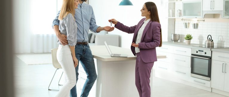 Female real estate agent giving house key to couple indoors